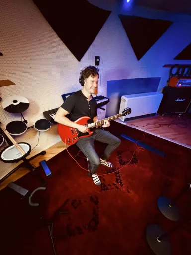 Mann spielt E-Gitarre in einem Musikstudio. Rote Gitarre, entspannte Atmosphäre.