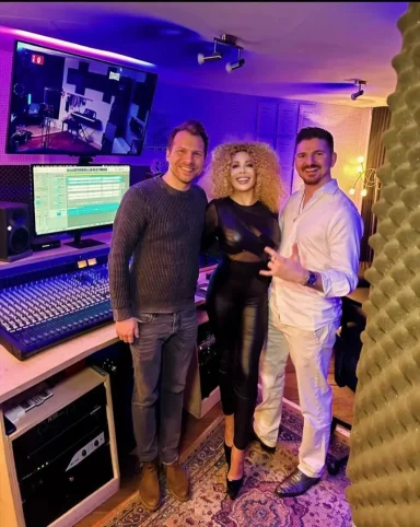 Drei Personen in einem Tonstudio, umgeben von Equipment und buntem Licht.