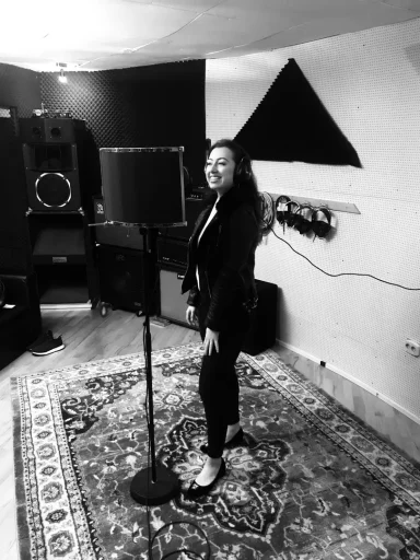 Frau steht lächelnd vor einem Mikrofon in einem Musikraum mit Teppich.