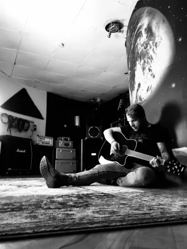 Junger Mann sitzt auf dem Boden und spielt Gitarre in einem kreativen Raum.