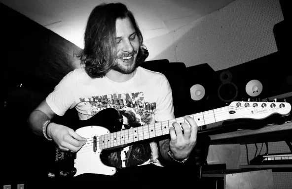 Mann mit Gitarre lächelt in einem Aufnahmestudio.