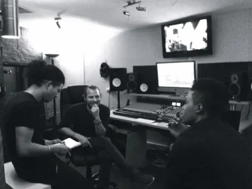Drei Personen in einem Tonstudio, Gespräch und Musikproduktion im Gange.
