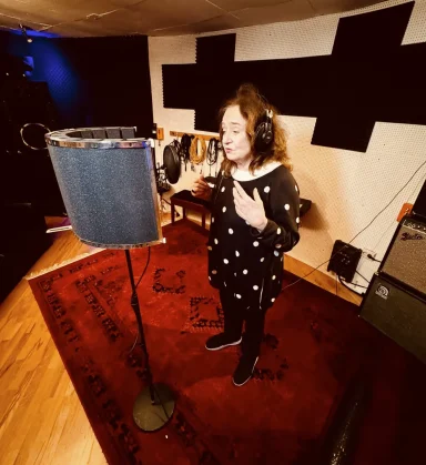 Eine Sängerin im Studio, die in ein Mikrofon singt, umgeben von Musikinstrumenten.