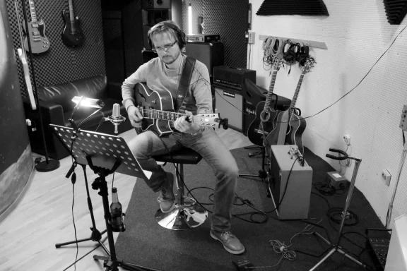 Mann spielt E-Gitarre im Studio, umgeben von Musikinstrumenten.