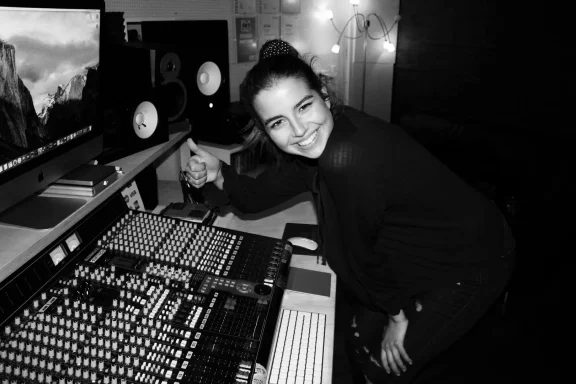 Eine lächelnde Person, die an einem Mischpult in einem Tonstudio arbeitet.