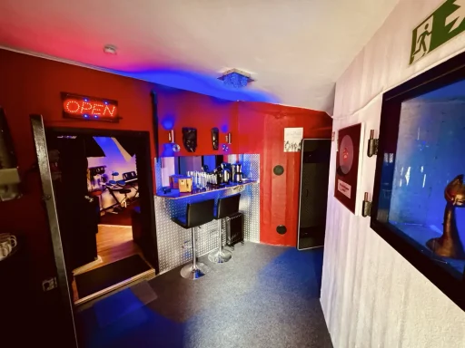 Innenraum eines Raumes mit roten Wänden, beleuchtet in Blau und lila, an einer Bar.