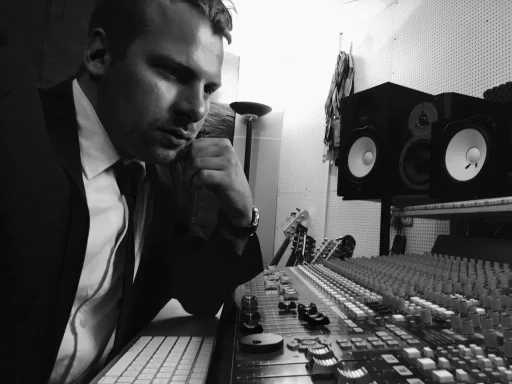 Mann in Anzug sitzt nachdenklich an Mischpult in Tonstudio.