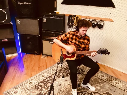 Mann spielt Gitarre in einem Aufnahmestudio, umgeben von Verstärkern.