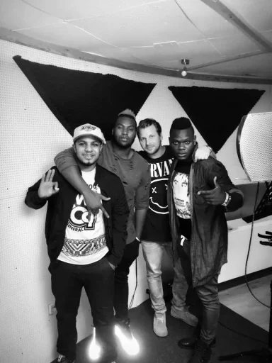 Vier Männer posieren lächelnd vor einer monochromen Wand mit geometrischen Formen.