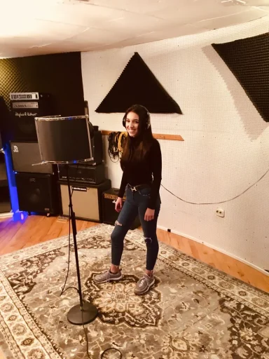 Junge Frau steht vor einem Mikrofon in einem Musikstudio mit Verstärkern.