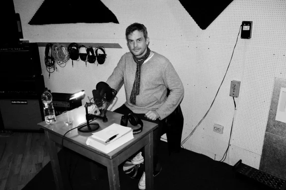 Mann sitzt an einem Tisch mit einem Mikrofon, Notizen und einem Headset in einem Studio.