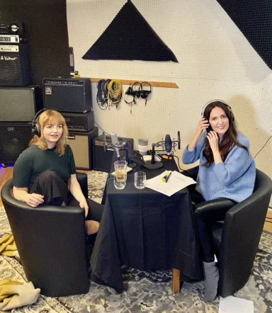 Zwei Frauen sitzen an einem Tisch in einem Tonstudio, umgeben von Musikgeräten.