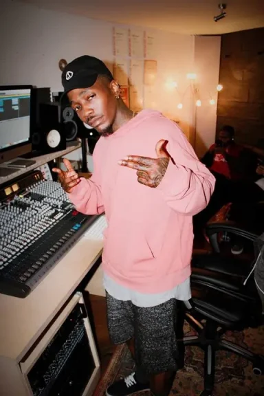Junger Mann in einem Tonstudio, trägt ein rosa Sweatshirt und posiert mit den Fingern.