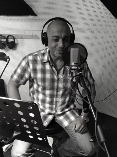 Mann mit Kopfhörern spricht ins Mikrofon, trägt kariertes Hemd.