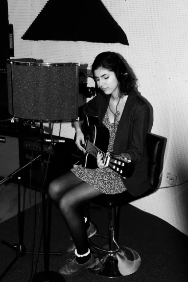 Junge Frau sitzt auf einem Stuhl und spielt Gitarre in einem Studio.