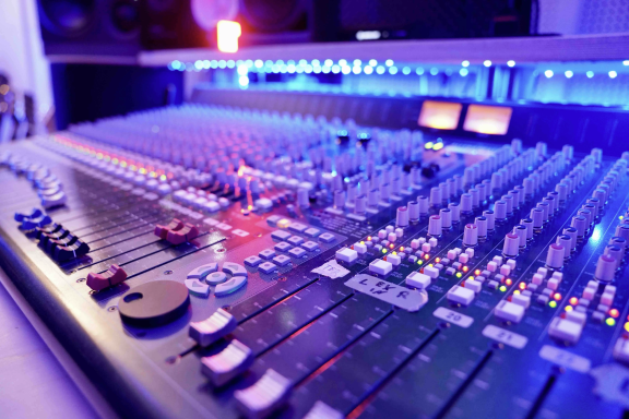 Mischpult mit bunten Lichtern und vielen Reglern im Vordergrund.