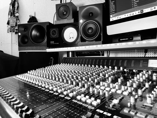 Schwarze und weiße Aufnahme eines Mischpults mit Lautsprechern im Hintergrund.
