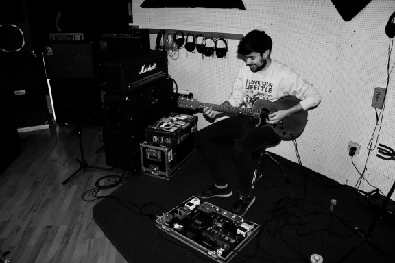 Mann spielt Gitarre in einem Musikstudio, umgeben von Equipment.