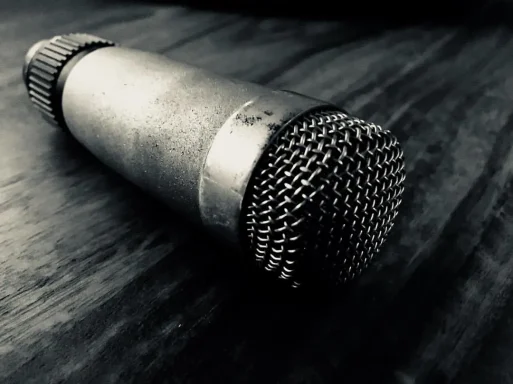 Ein silbernes Mikrofon liegt auf einer dunklen Holzoberfläche.