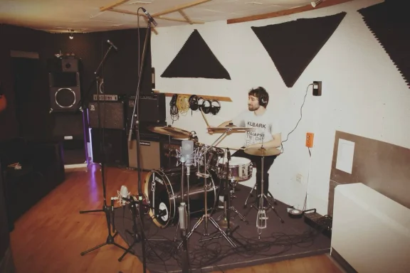 Ein Musiker am Schlagzeug in einem gut beleuchteten Probenraum.