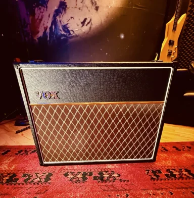 Ein Vox Gitarrenverstärker auf einem Teppich vor einer dunklen Wand.