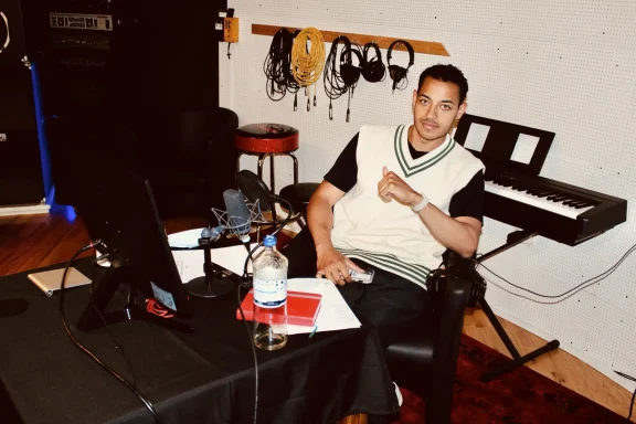 Person sitzt in einem Studio, umgeben von Musikgeräten und Notizen.