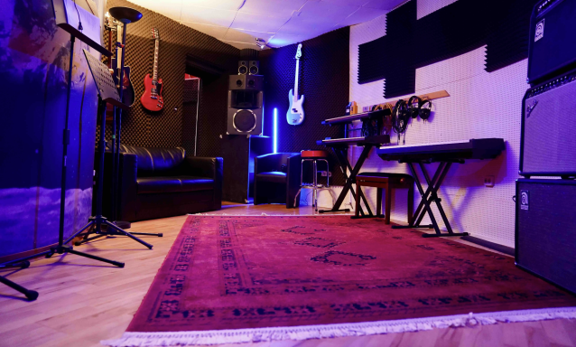 Ein Musikraum mit Gitarren, Keyboard, Verstärkern und einem roten Teppich.