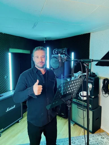 Mann in einem Aufnahmestudio gibt Daumen nach oben neben Mikrophon und Lautsprechern.