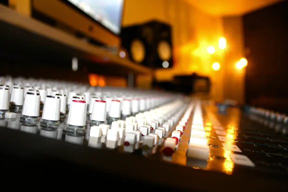 Ein Blick auf ein Mischpult mit Reglern und unscharfem Hintergrund im Aufnahmestudio.