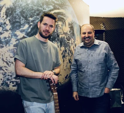 Zwei Männer stehen in einem Aufnahmestudio, einer hält eine Gitarre, Hintergrund mit Erde.