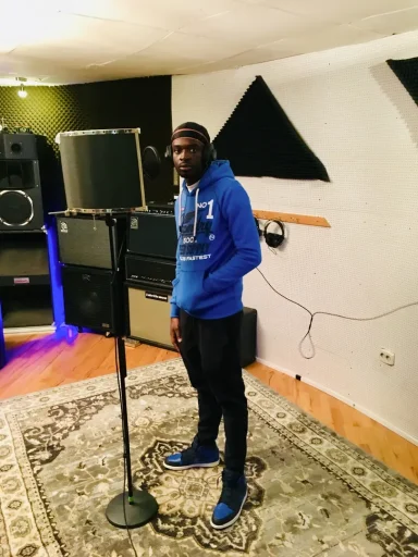 Ein Sänger steht im Studio vor einem Mikrofon, umgeben von Musikgeräten.