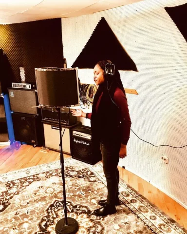 Eine Person steht im Aufnahmestudio vor einem Mikrofon und trägt Kopfhörer.