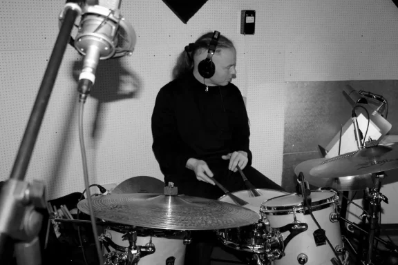 Mann am Schlagzeug in einem Tonstudio, Mikrofone im Hintergrund.