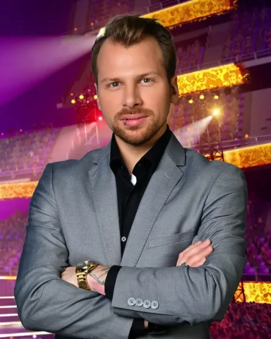 Mann im grauen Anzug mit verschränkten Armen vor einer beleuchteten Bühne.