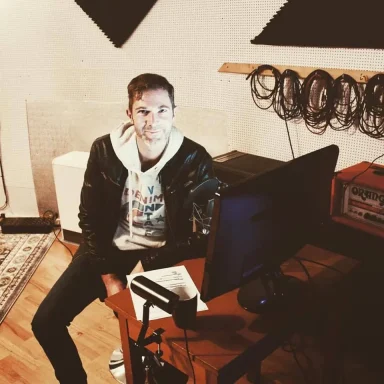 Junger Mann sitzt an einem Tisch mit Computer in einem Aufnahmestudio.