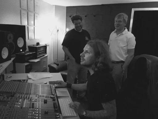 Drei Männer im Tonstudio, einer steuert ein Mischpult, die anderen schauen zu.