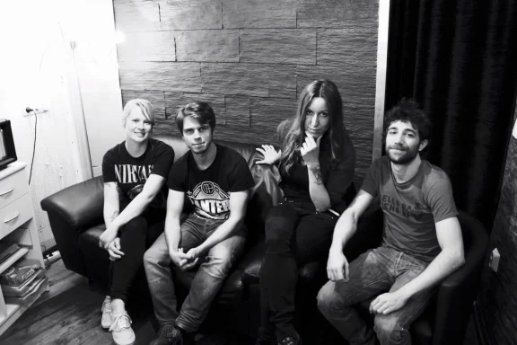 Vier Personen sitzen entspannt auf einer Couch in einem dunklen Raum.