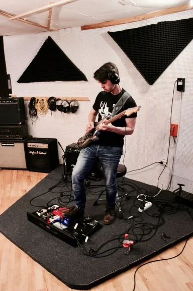 Ein Musiker spielt E-Gitarre in einem Tonstudio mit Effektpedalen im Vordergrund.