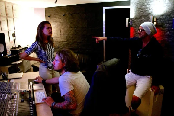 Drei Personen in einem Musikstudio, die eine Diskussion führen und an einem Mischpult arbeiten.