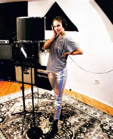 Frau im Tonstudio, trägt graues T-Shirt und glänzende, silberne Hose.