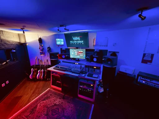 Musikstudio mit bunten Lichtern, Mischpult, Monitor und Instrumenten.