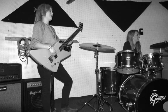 Zwei Musikerinnen: eine spielt E-Gitarre, die andere sitzt am Schlagzeug.
