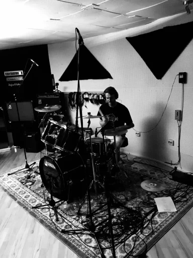 Ein Musiker sitzt in einem Studio und spielt Schlagzeug auf einem Teppich.