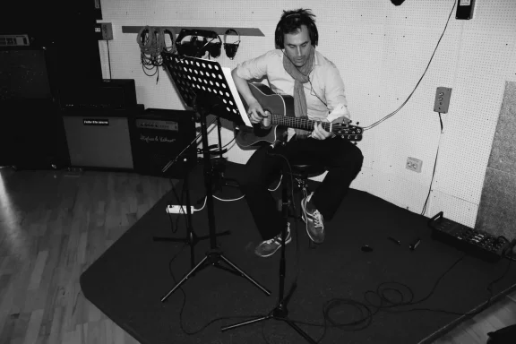 Musiker sitzt mit einer Gitarre in einem Aufnahmestudio und spielt.