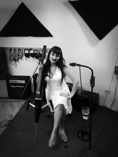 Frau in einem weißen Kleid sitzt im Studio, mit Mikrofon und Instrument.