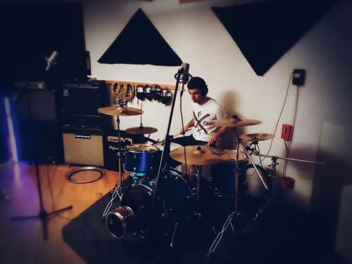 Ein Schlagzeuger spielt in einem Aufnahmestudio. Hinter ihm befinden sich Musikanlagen.