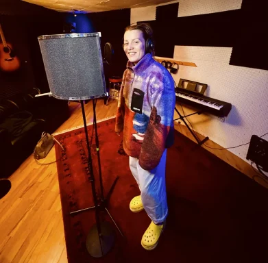 Person im Aufnahmestudio mit Mikrofon, lässiger Kleidung und gelben Schuhen.