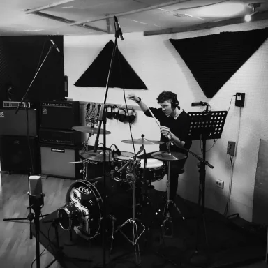 Ein Schlagzeuger spielt in einem Aufnahmestudio. Mikrofone und Verstärker sind sichtbar.